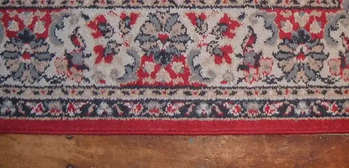 The edge of a red rug: three border stripes and the bound selvedge meeting the floorboards